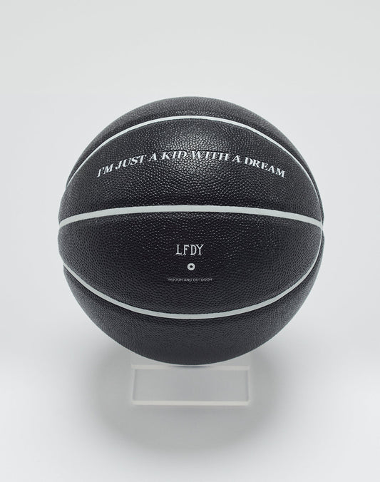 A Live Fast Basketball from LIVE FAST DIE YOUNG, black with white stripes and deep grooves, sits on a clear stand. It features IM JUST A KID WITH A DREAM, the initials LFDY, and small extra text below.