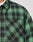 Close-up of a person wearing the LIVE FAST DIE YOUNG LFDY Padded Flannel, an oversized green and black plaid overshirt with chest pockets, a small tag on the pocket seam, and a white undershirt visible for a relaxed style.