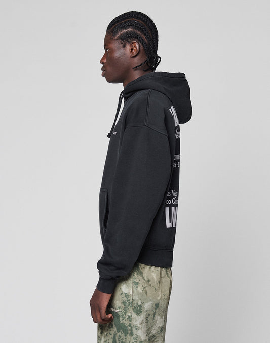 A person with braided hair stands in profile, wearing the LIVE FAST DIE YOUNG Live Fast Vegas Hooded in an oversize fit with front and back prints, paired with white and green camouflage pants (65% Baumwolle), against a light gray background.