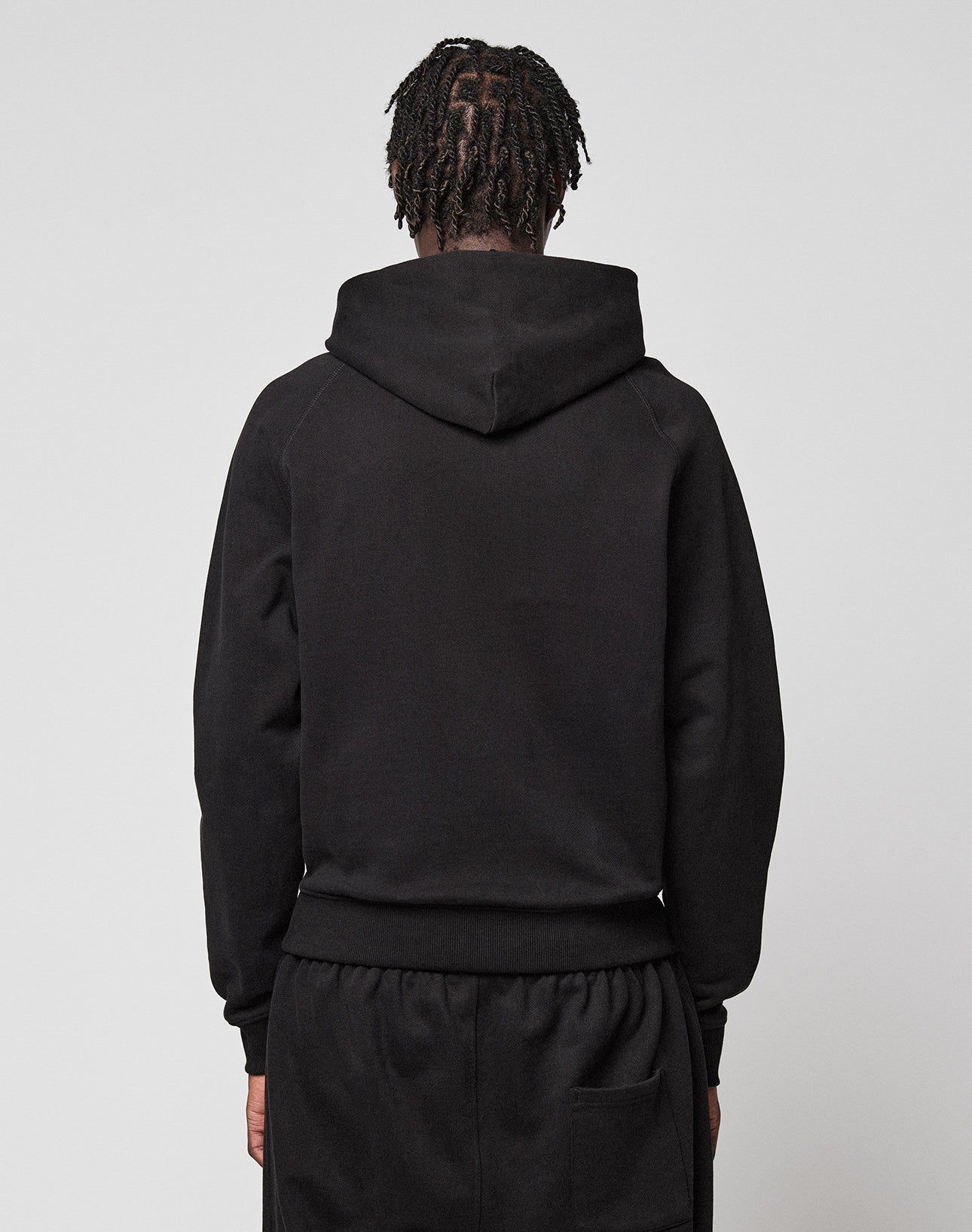 A person with braided hair stands with their back to the camera, wearing a black LFDY Embroidery Hooded by LIVE FAST DIE YOUNG and matching black pants against a plain light background.