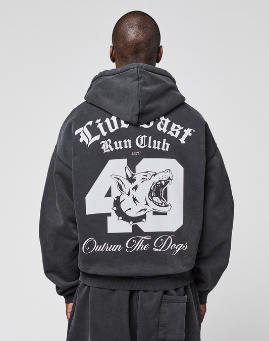 Someone wearing the LIVE FAST DIE YOUNG LFDY Run Club Hooded Zip, a black oversized hoodie featuring bold white graphics on the back: "Live Fast Run Club," "49," "Outrun The Dogs," and a snarling dog head. Made from cotton-polyester. | model