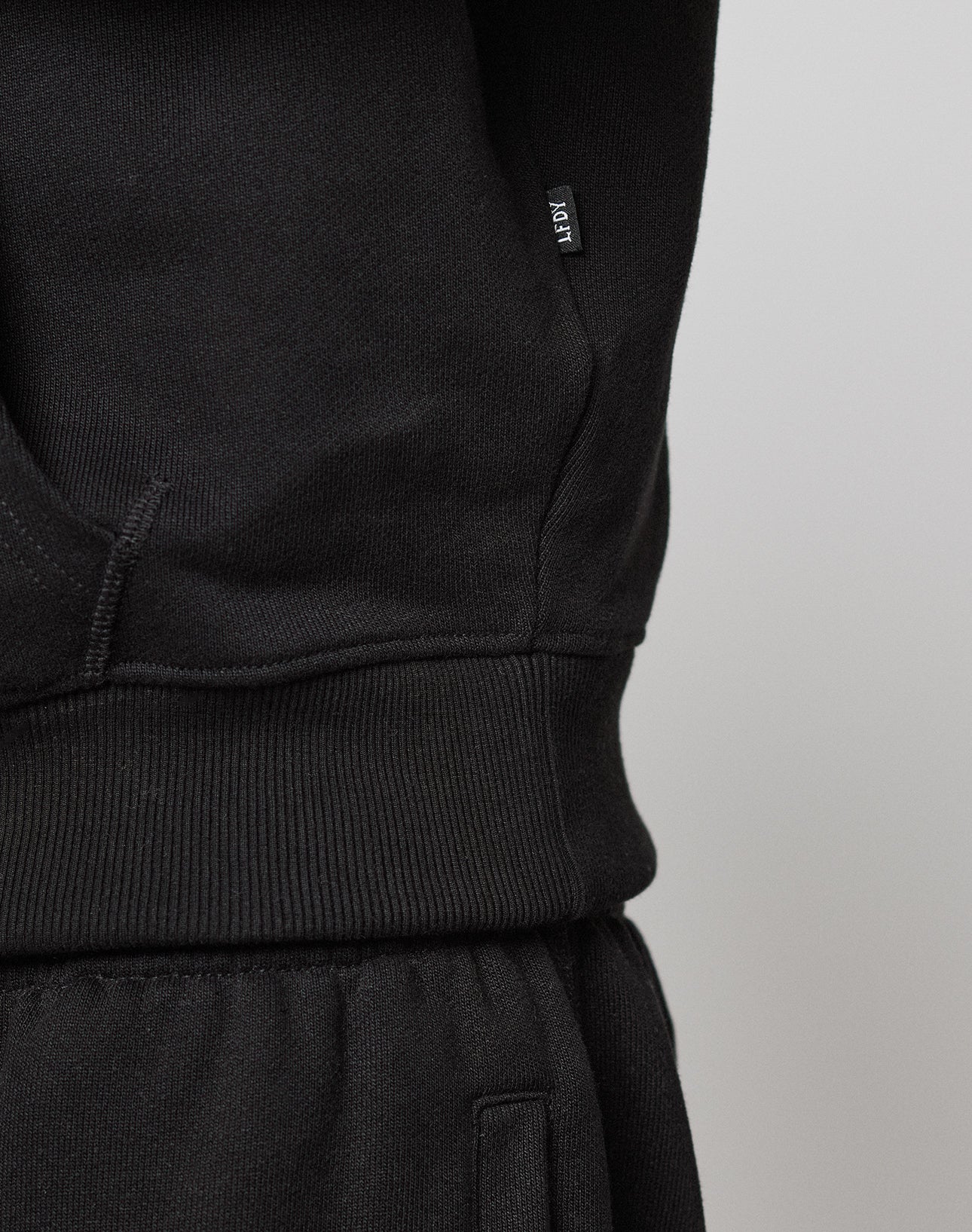 Close-up of a black LFDY Embroidery Hooded by LIVE FAST DIE YOUNG, focusing on the waistband. A small black tag with white "ICON" text is sewn into the side seam of the 100% Baumwolle regular fit hoodie.