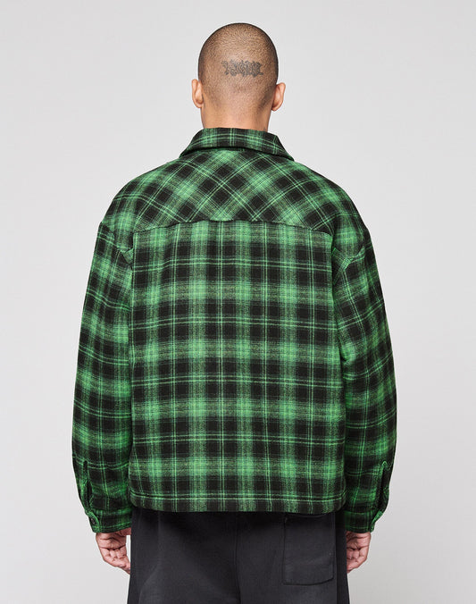 A person with a shaved head and visible tattoo faces away, wearing a green and black LIVE FAST DIE YOUNG LFDY Padded Flannel and black pants against a plain light background.