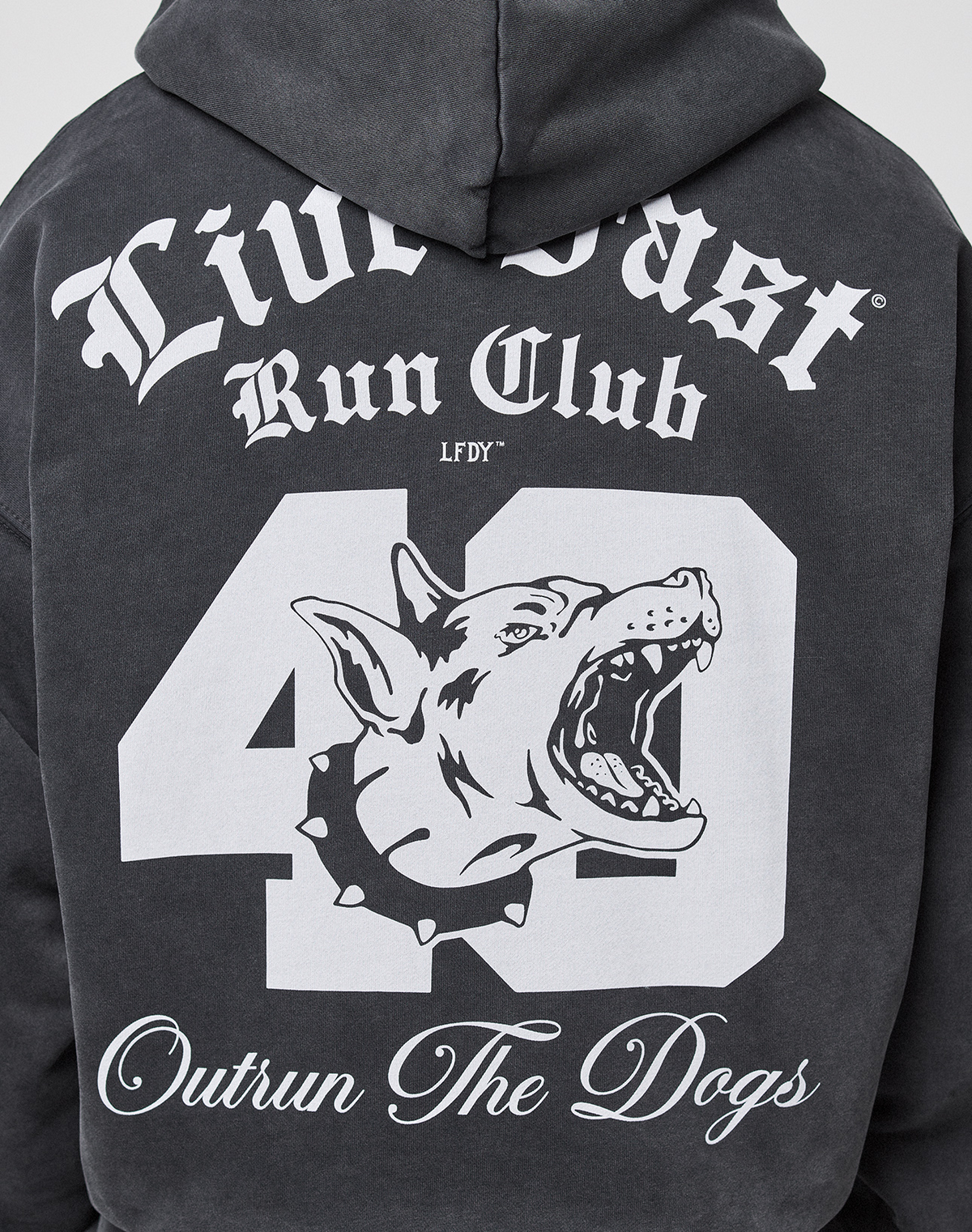 A person wears the LIVE FAST DIE YOUNG LFDY Run Club Hooded Zip, an oversize dark hoodie with bold white “Live Fast Run Club” and “Outrun The Dogs” prints, a large number 40, snarling dog graphic on the back, and a stylish sleeve print.
