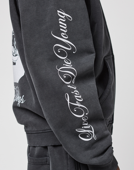 Wearing the LFDY Run Club Hooded Zip by LIVE FAST DIE YOUNG, a person poses with their hand in their pocket. The black oversize sweatshirt features a white cursive Ärmelprint reading "Live Fast Die Young." Only part of their torso and arm is visible.