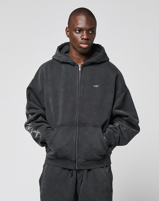 A person wearing the LIVE FAST DIE YOUNG LFDY Run Club Hooded Zip with chest LFTY text, Ärmelprint details, and matching oversized sweatpants stands with hands in pockets against a plain light gray background.
