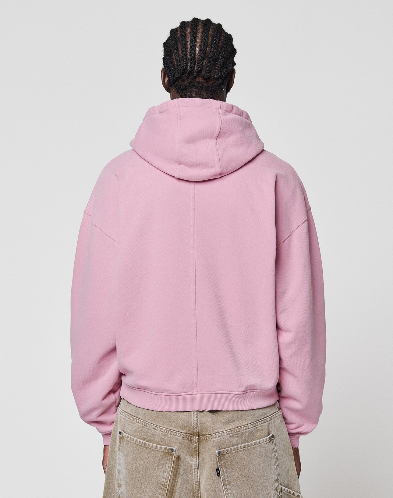A person with braided hair, seen from behind, wears the LIVE FAST DIE YOUNG LFDY Vandals Hooded Zip in light pink and beige pants, standing against a plain white background.