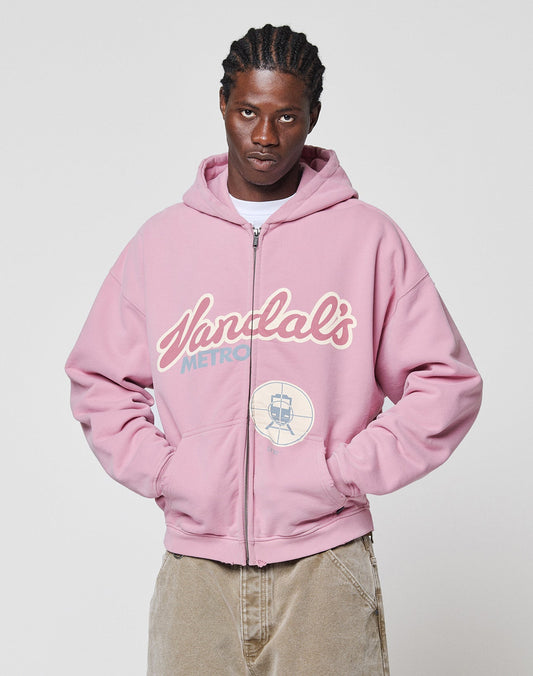 A person with braided hair wears the LFDY Vandals Hooded Zip by LIVE FAST DIE YOUNG—a pink oversize zip-up jacket with a bold METRO and train frontprint—standing against a plain light background, hands in pockets.