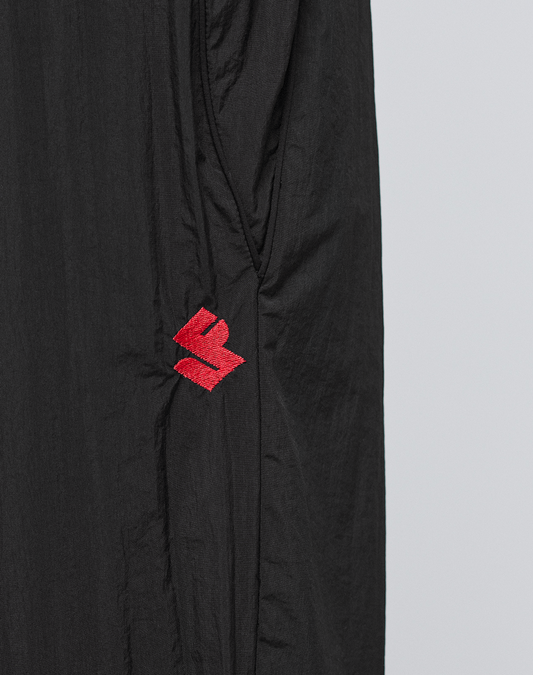 Close-up of lightweight, slightly crinkled polyamid fabric on the LFDY Dealership Trackpants by LIVE FAST DIE YOUNG, featuring a small red abstract embroidered logo near the left side seam.