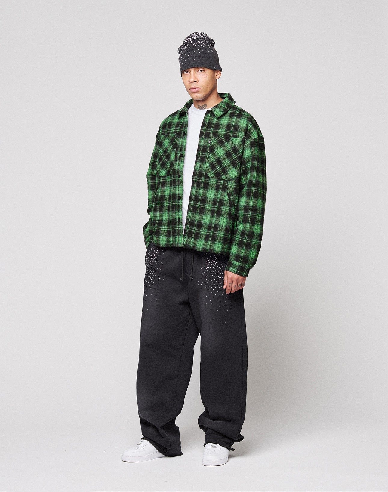 A person in a gray beanie, white shirt, loose black pants, white sneakers, and the LIVE FAST DIE YOUNG LFDY Padded Flannel stands against a plain light background.