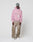 A person in a pink LFDY Vandals Hooded Zip by LIVE FAST DIE YOUNG with oversize fit and unique distressing, brown loose pants with light patches, white sneakers, and a printed cap stands against a plain white background.