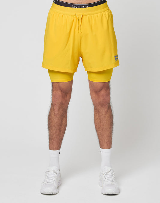 A person wearing LIVE FAST DIE YOUNG Live Fast Performance Running Shorts with integrierte Tights, white socks, and white sneakers, standing against a plain white background.