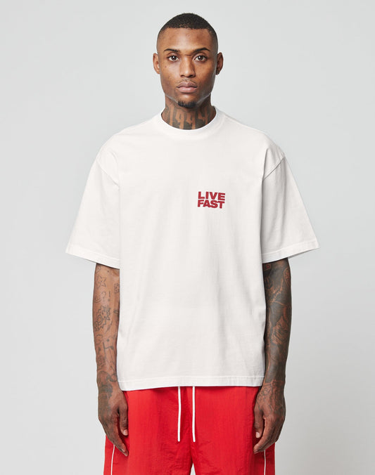 A tattooed person wears the oversize white LFDY 4 Ever Tee by LIVE FAST DIE YOUNG, featuring LIVE FAST red front and back print, paired with bright red shorts against a plain light background.