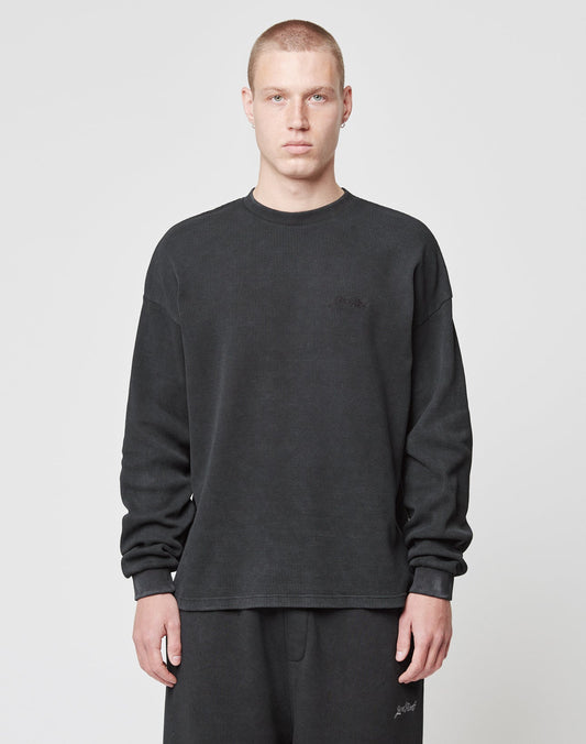 A person with short hair stands against a white background, wearing the LIVE FAST DIE YOUNG Basic Script Waffle Longsleeve and matching black pants. The 100% Baumwolle outfit features a subtle Logo-Stick, hands by their sides.