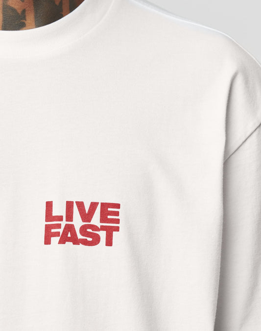 Close-up of the LFDY 4 Ever Tee by LIVE FAST DIE YOUNG, an oversized white cotton T-shirt with bold red LIVE FAST lettering on the front. A tattooed neck and shoulder are visible at the top left.