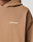 A close-up of the Live Fast Plain Hooded by LIVE FAST DIE YOUNG in tan, oversize fit, with LIVE FAST™ in white on the chest. Only part of the wearer’s shoulder, neck, and hood can be seen.