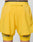 A person wears LIVE FAST DIE YOUNG Live Fast Performance Running Shorts in bright yellow, featuring lightweight fabric, a zippered back pocket, and integrated tights with LIVE and FAST printed in gray near each hem.