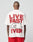 A person faces away in the LFDY 4 Ever Tee by LIVE FAST DIE YOUNG—an oversized white cotton shirt with bold red LIVE FAST 4 EVER front and back prints and a large outlined 4 on the back, paired with matching red shorts.