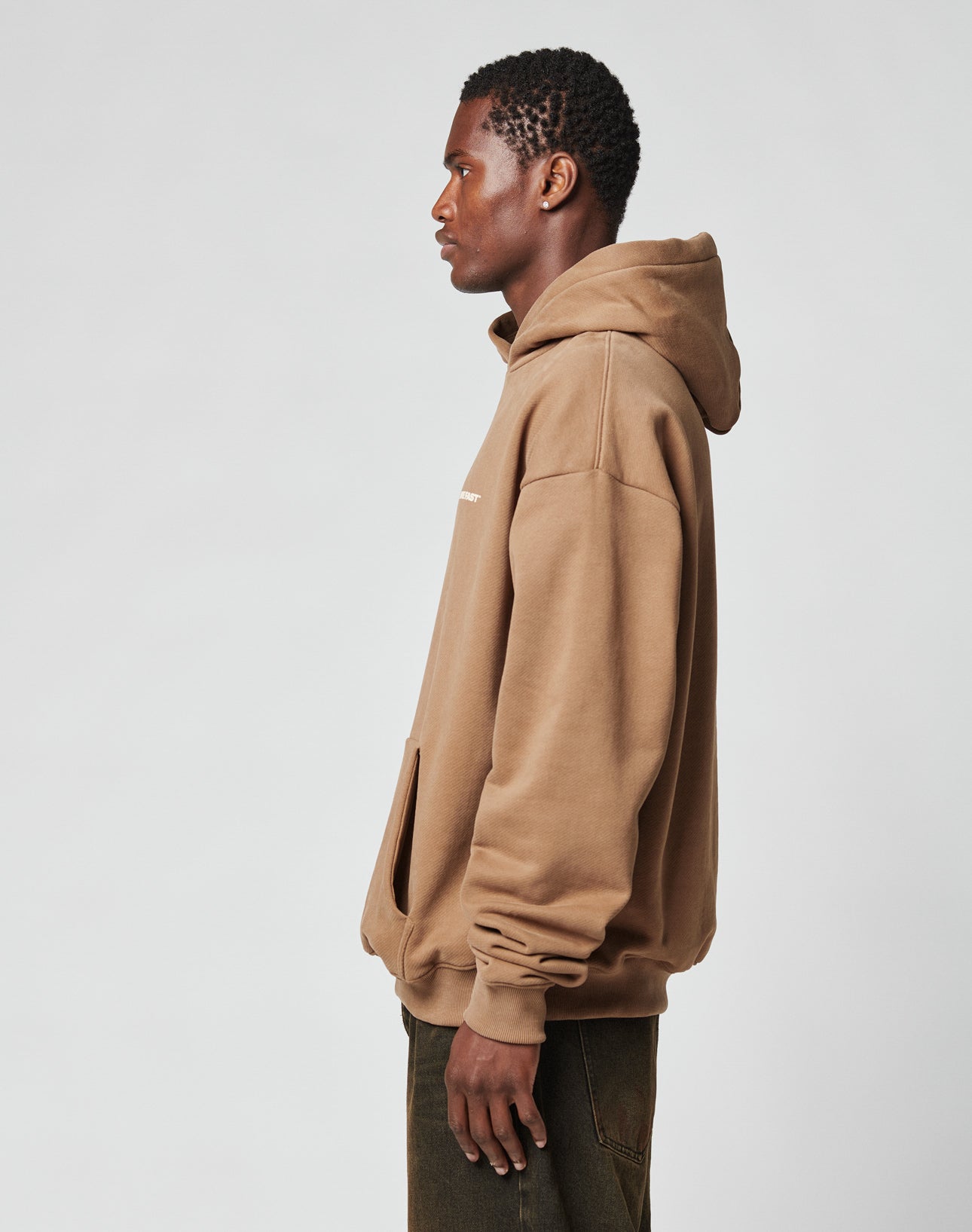 A person stands in profile against a plain light gray background, wearing the LIVE FAST DIE YOUNG Live Fast Plain Hooded sweatshirt in an Oversize Fit and dark pants, with their hands relaxed by their sides.