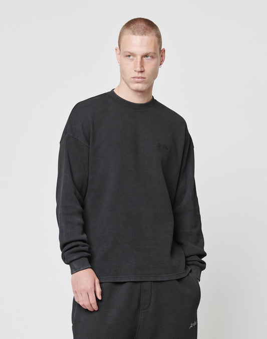 A person with short hair wears the LIVE FAST DIE YOUNG Basic Script Waffle Longsleeve in black with matching black pants, standing against a plain white background and looking slightly to the side with a neutral expression.