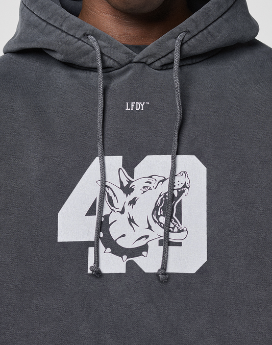 A close-up of a person wearing the LFDY 40 Hooded by LIVE FAST DIE YOUNG, a dark gray oversize-fit hoodie with LFDY above a white 40 and an illustrated snarling dog’s head, made from soft cotton-polyester blend.