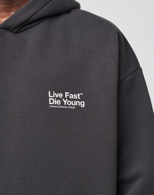 Close-up of the LIVE FAST DIE YOUNG Live Fast NY Hooded in dark gray, Oversize Fit, with white front and back print. Only part of the neck and shoulder is visible. Made from 70% cotton. Limited Collection ©2023.