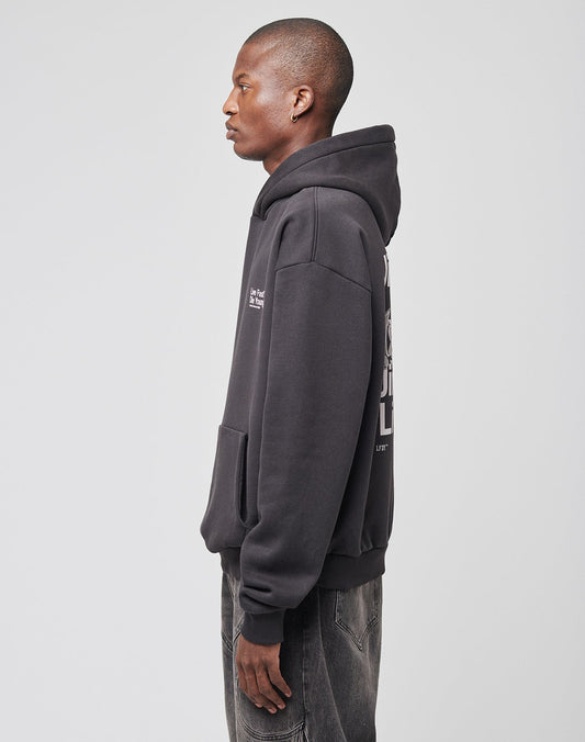 A person stands in profile facing left, wearing the LIVE FAST DIE YOUNG Live Fast NY Hooded in oversize fit with a front pocket, paired with faded black jeans, set against a plain light gray background.