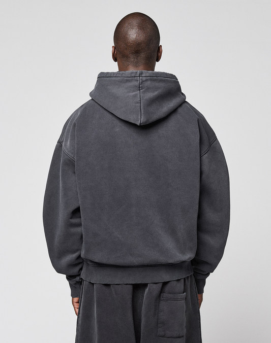 A person with a shaved head stands with their back to the camera, wearing the LFDY 40 Hooded oversize-fit dark gray sweatshirt and matching pants by LIVE FAST DIE YOUNG. The set features a kangaroo pocket and is made from cotton-polyester. The background is plain and light.