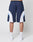 A person is shown from the back against a white background, wearing LIVE FAST DIE YOUNG Basic Trackshorts in navy with white and light blue accents, logo print, elastic waistband, paired with white crew socks and sneakers. Only lower half visible.
