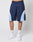 Someone is wearing LIVE FAST DIE YOUNG Basic Trackshorts in navy blue with light blue and white panels, featuring an elastic waistband, paired with white LEDY socks and white sneakers, standing against a plain light background.