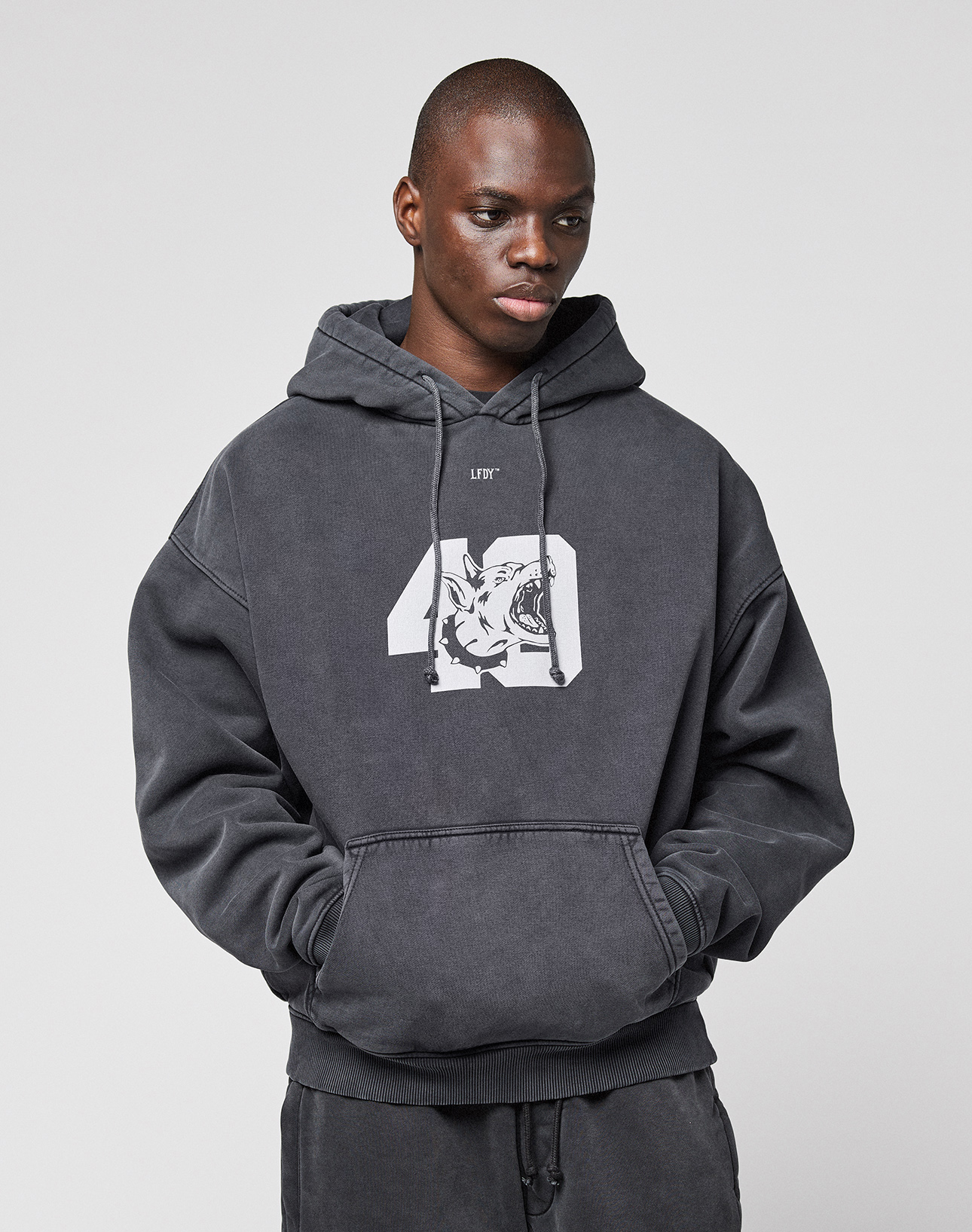 A person wearing the LFDY 40 Hooded by LIVE FAST DIE YOUNG, featuring a dark gray oversize fit with a white "40" and tiger graphic plus cozy Kangaroo-Tasche, stands against a plain light background.
