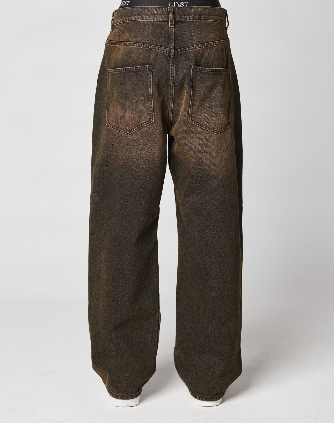 The LFDY Baggy Denim by LIVE FAST DIE YOUNG features a loose, high-waisted brown fit with two large back pockets, subtle faded details, a flag label, and is styled with visible white shoes at the hem.