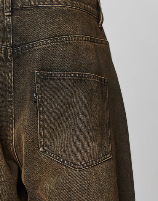 Close-up of the back pocket of LFDY Baggy Denim by LIVE FAST DIE YOUNG, featuring faded brown denim, baggy fit, visible stitching details, and a small black flag label on the pocket side.
