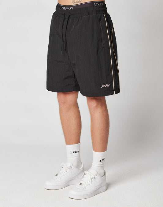 A person wearing LIVE FAST DIE YOUNG Beach Shorts, white crew socks with LFDY text, and white Nike sneakers stands against a plain light background.