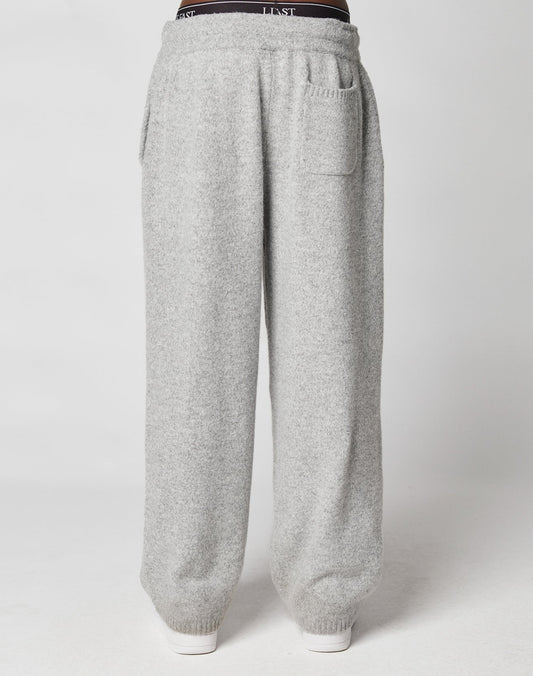 A person wearing LIVE FAST DIE YOUNG Live Fast Boucle Pants in a wide fit and light gray color with an elastic waistband and front pockets, standing against a plain white background.