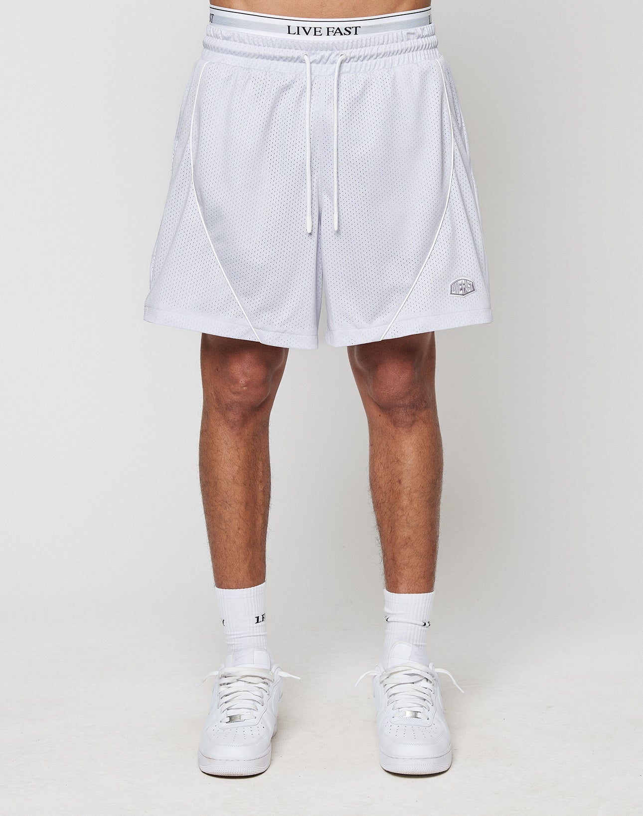 A person in LFDY Piping Mesh Shorts by LIVE FAST DIE YOUNG, featuring a white mesh design, LIVE FAST Elastikbund waistband, small logo near the hem, white crew socks, and sneakers stands against a plain background.
