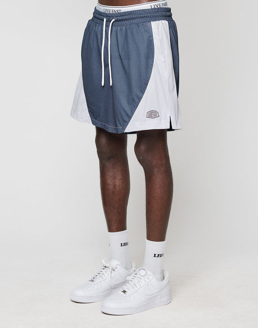 A person wears blue and white LFDY Piping Mesh Shorts by LIVE FAST DIE YOUNG with a LIVE FAST waistband, white socks with LED text, and white Nike sneakers, standing against a plain white background. | model