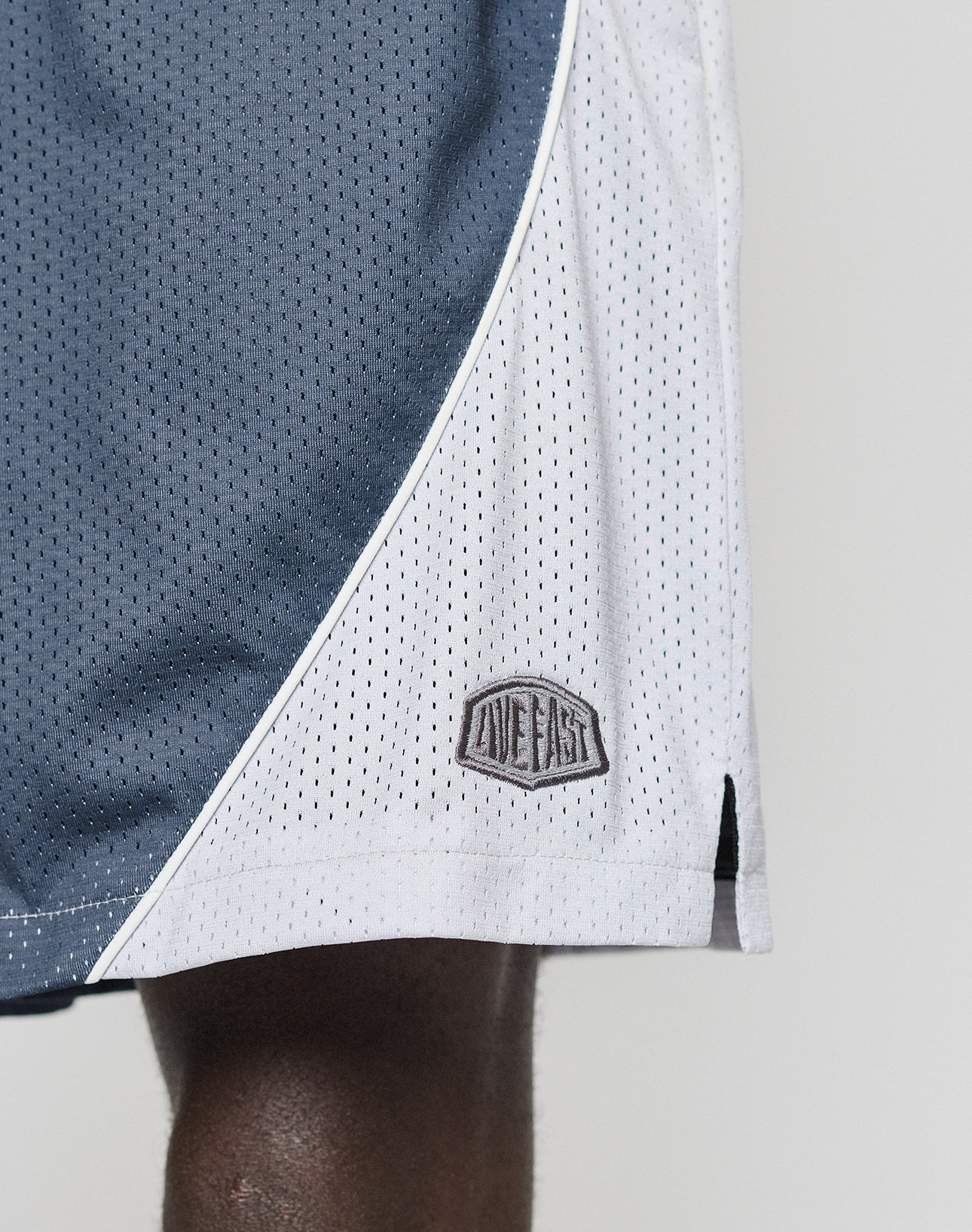 Close-up of a person wearing LFDY Piping Mesh Shorts by LIVE FAST DIE YOUNG, featuring gray and white mesh polyester, an elastic waistband, LIVE EASY stitched on the lower side, and a regular fit. Only part of the upper leg is visible.