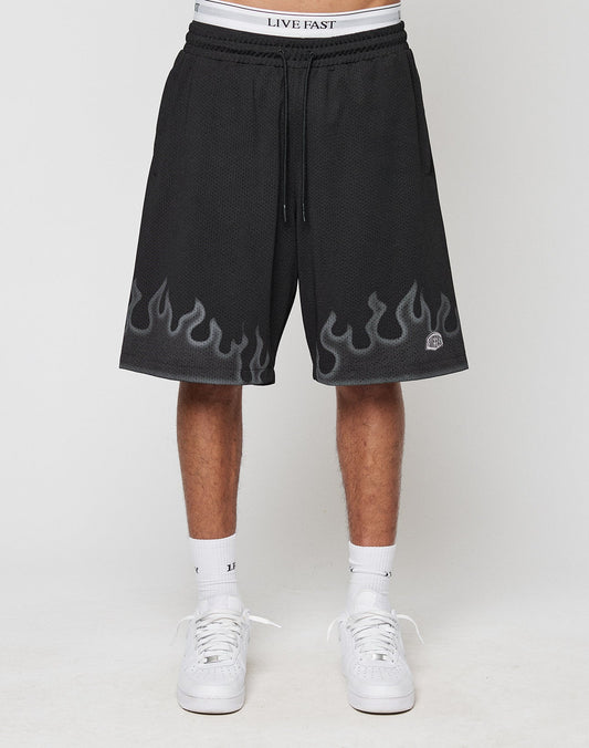 A person wears LIVE FAST DIE YOUNG Burning Mesh Shorts with gray flame print along the hem, LIVE FAST on the elastic waistband, paired with white socks and sneakers. Photo shows a plain background.