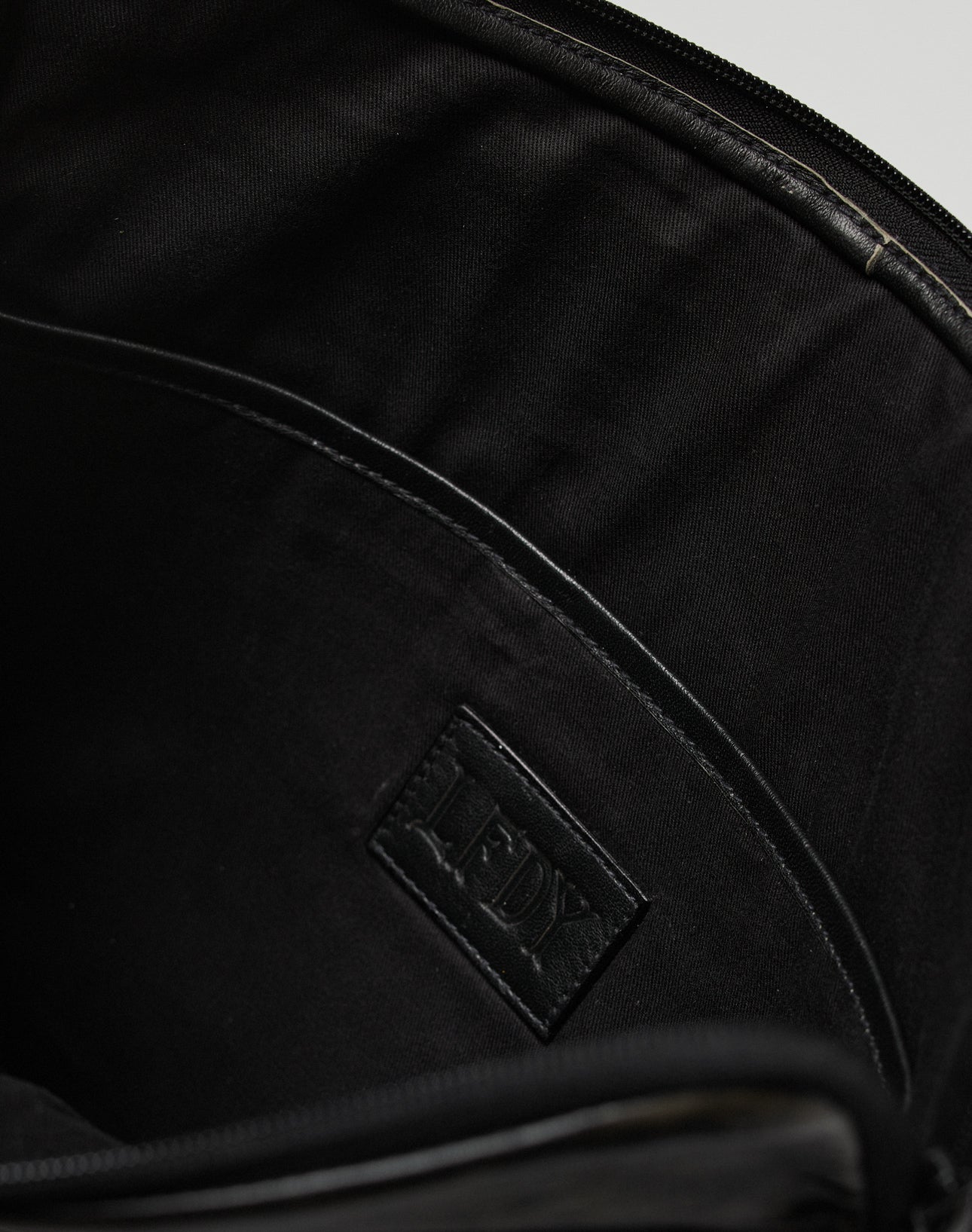 Close-up of the LFDY Laptop Leather Case by LIVE FAST DIE YOUNG, showing its fabric-lined black interior, embossed LFDY logo patch, visible zipper details, and a practical inner pocket.