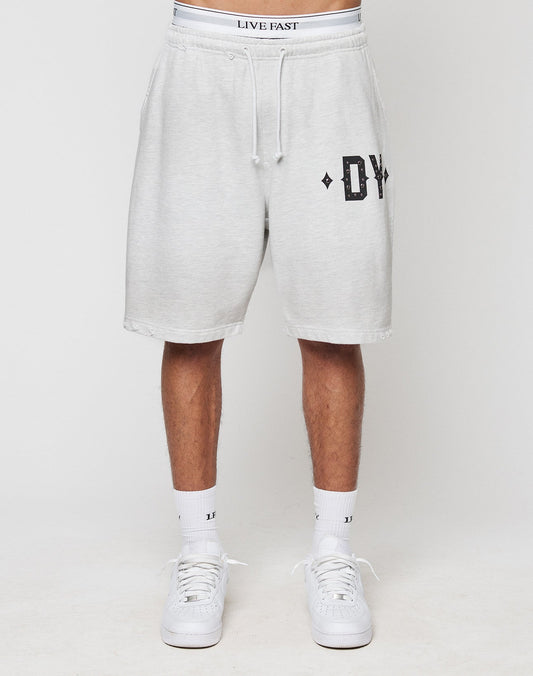 Someone stands against a plain background wearing DY Rivet Shorts by LIVE FAST DIE YOUNG—light gray, oversize fit with DY on the left leg, a white waistband featuring LIVE FAST, paired with white socks and sneakers.