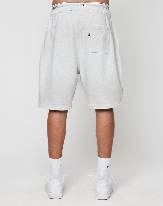 A person faces away, wearing LIVE FAST DIE YOUNGs DY Rivet Shorts in light gray with a back pocket and LEISURE-print waistband. Made from 100% Baumwolle, theyre paired with white socks and sneakers for comfort and style.