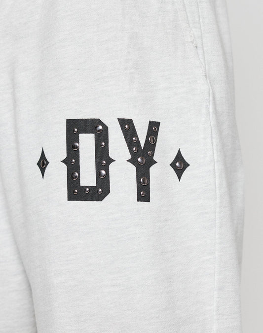 Close-up of DY Rivet Shorts by LIVE FAST DIE YOUNG, in light gray and oversize fit. Features large black DY letters with metallic studs and diamond-shaped accents. Made from 100% Baumwolle, shown against a neutral background.