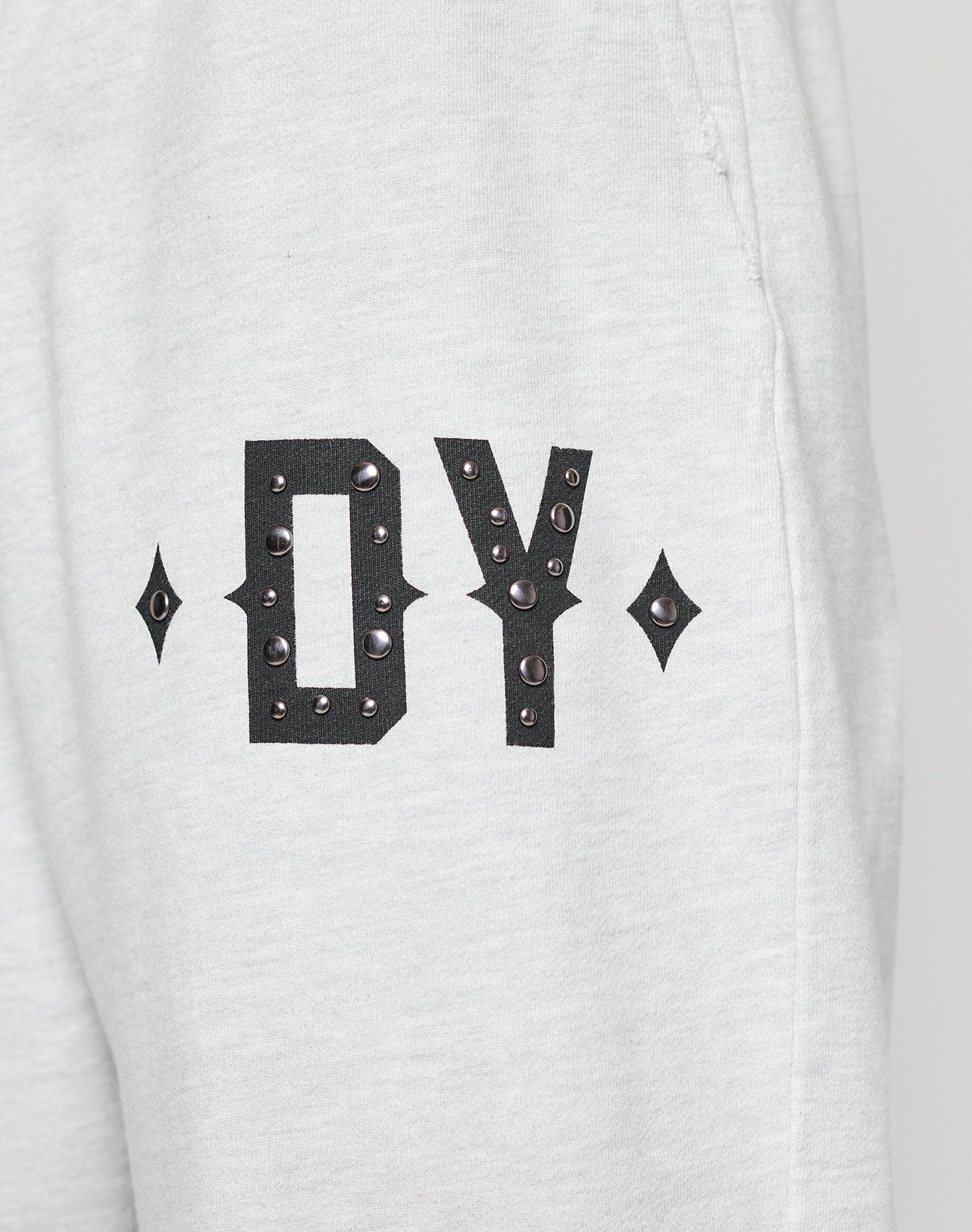 Close-up of DY Rivet Shorts by LIVE FAST DIE YOUNG, in light gray and oversize fit. Features large black DY letters with metallic studs and diamond-shaped accents. Made from 100% Baumwolle, shown against a neutral background.