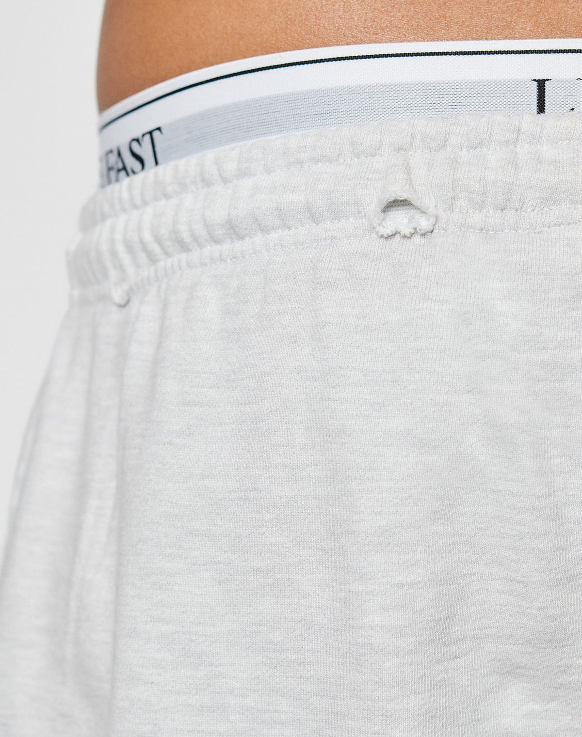 Close-up of the waistband and upper section of light gray DY Rivet Shorts by LIVE FAST DIE YOUNG in Oversize Fit, showing elastic band details and part of white underwear with a visible waistband and black text.