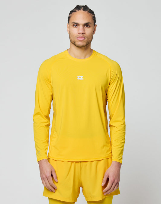 A person with braided hair stands against a plain light gray background, wearing the LIVE FAST DIE YOUNG Live Fast Performance Longsleeve in yellow and matching shorts, looking straight ahead with a neutral expression. | model