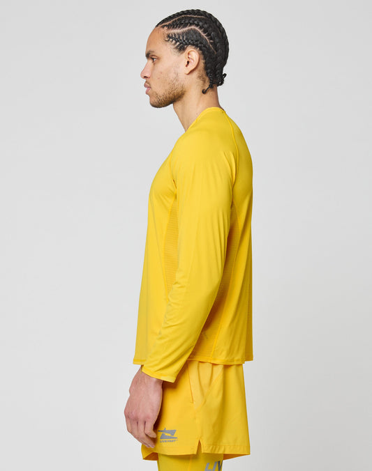 A man with braided hair is shown in profile, wearing the LIVE FAST DIE YOUNG Live Fast Performance Longsleeve and matching yellow shorts, standing against a plain light gray background.