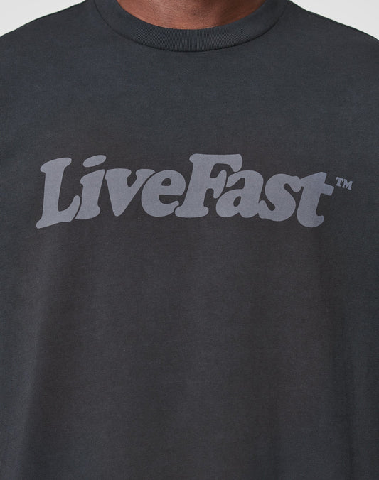A close-up of the LIVE FAST DIE YOUNG Basic Tee, a black, oversized cotton shirt with LiveFast™ in bold light gray across the chest and a vintage-wash finish for standout style.