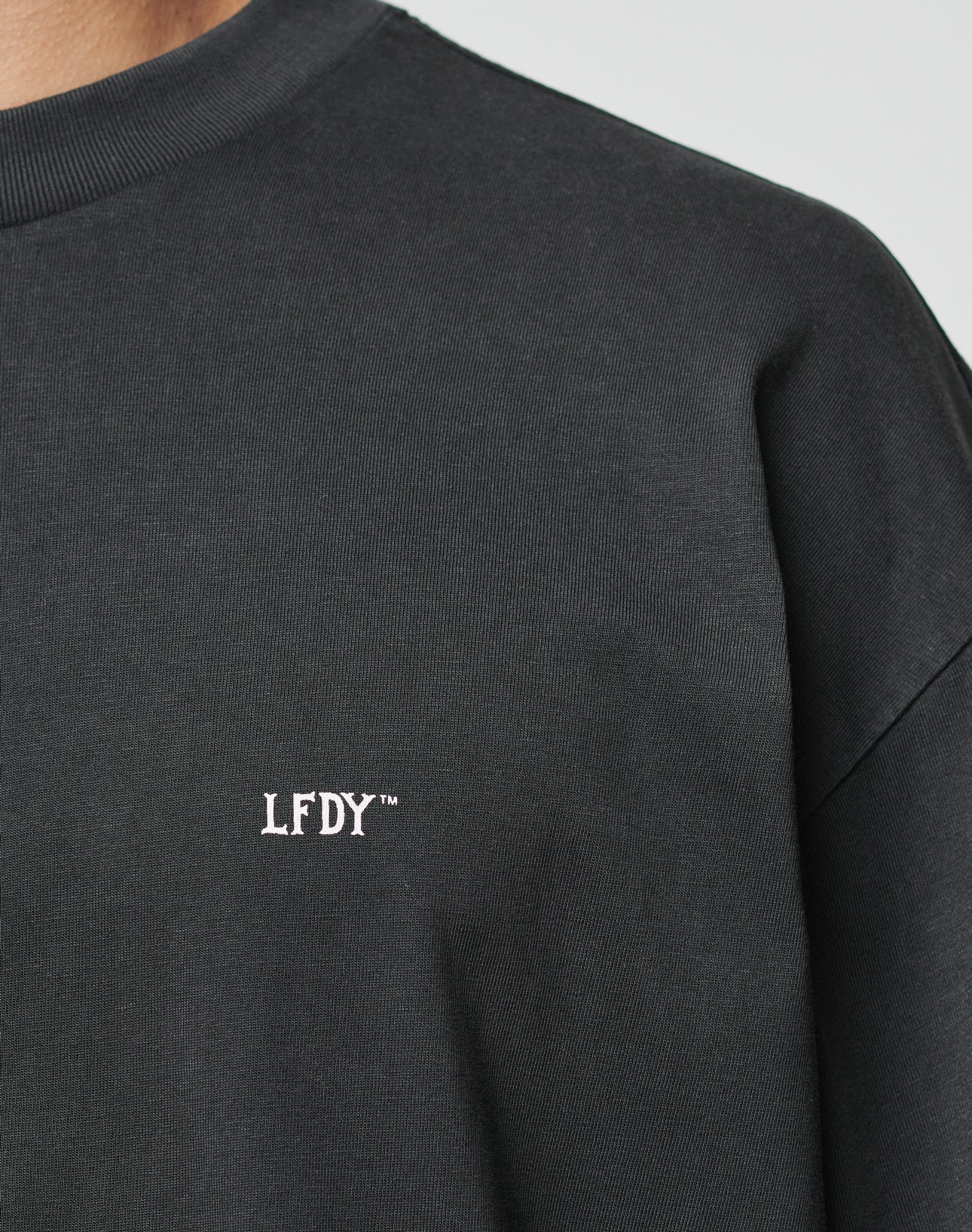 Close-up of a person wearing the Everybody Eats Tee by LIVE FAST DIE YOUNG, featuring LFDY™ embroidered in white on the left chest. Crafted from 100% Baumwolle for comfort and durability.