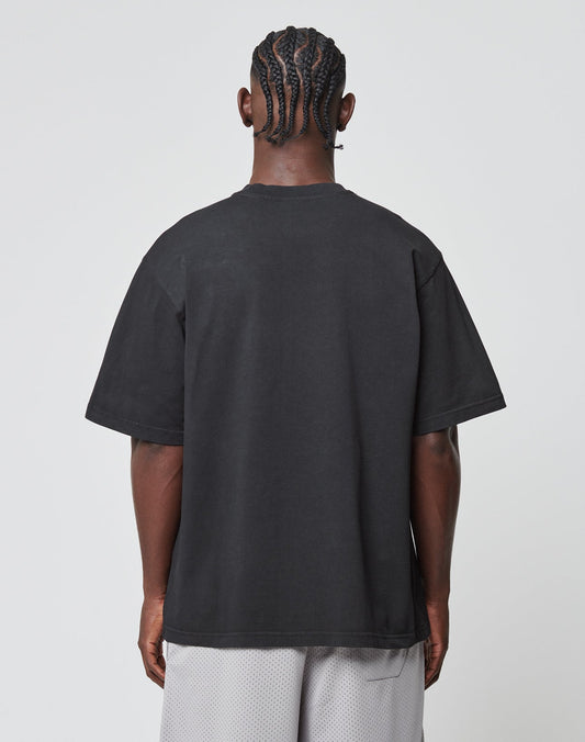 A person with braided hair is seen from behind in a LIVE FAST DIE YOUNG Basic Tee, an oversize fit black T-shirt made of 100% Baumwolle, paired with light gray mesh shorts, standing against a plain white background.